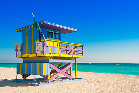 This is a stock photo from Shutterstock. This is a lifeguard station on Miami Beach. The lifeguard station is painted in bright colors. The ocean is in the background.